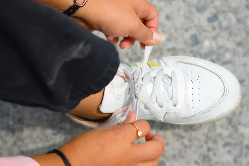 Zbliżenie na dłonie kobiety zawiązującej sznurówki białych sneakersów na zewnątrz.